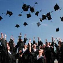 Group of graduates celebrating by throwing caps in the air during a sunny day.